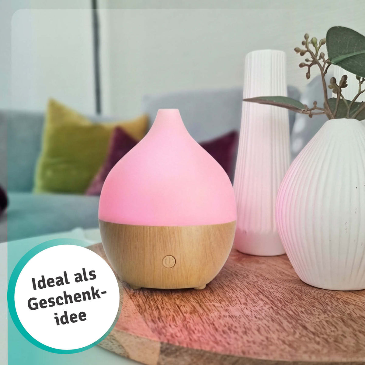 Kompakter Aroma USB Diffuser in weiß mit Holzsockel, neben ätherischen Ölen und dekorativen Kugeln auf einem Tisch.
