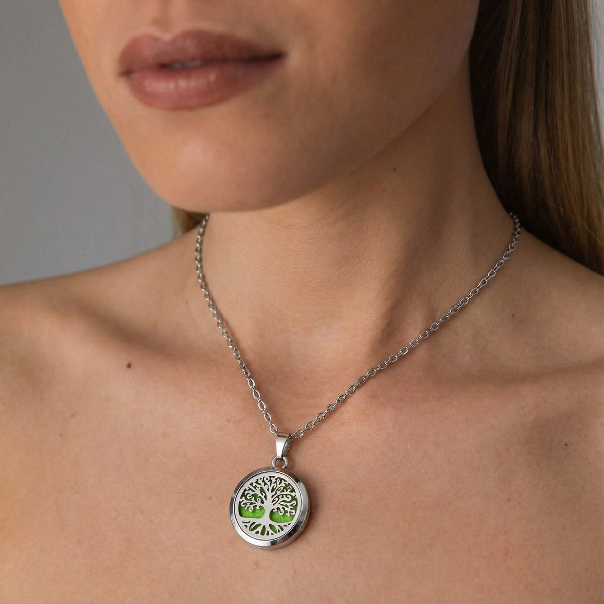 Diffuser necklace for essential oils featuring a silver medallion with a tree design and green accents, worn on a model.