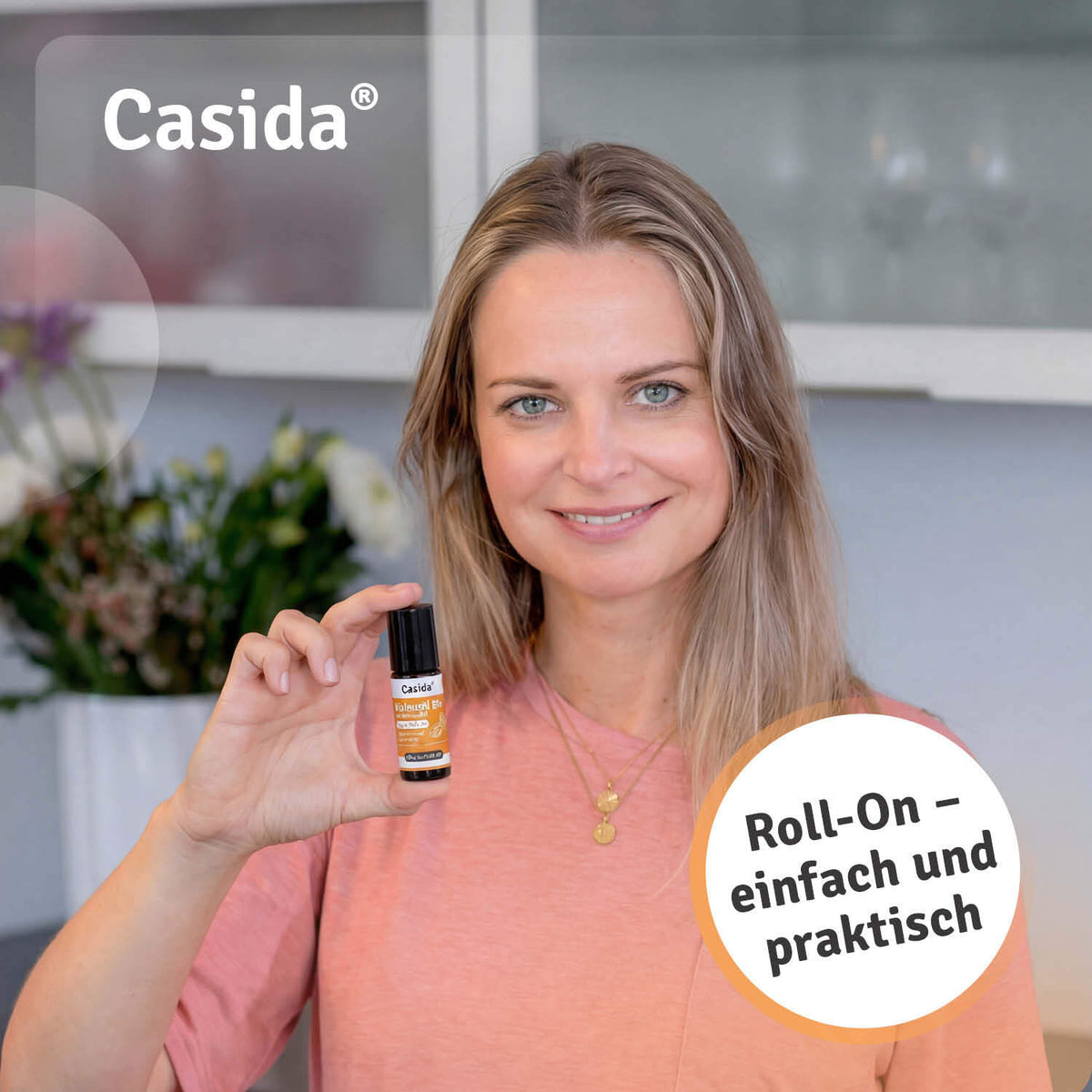 Casida bio castor oil roll-on with frankincense oil held by a woman, featuring a black cap and orange label.