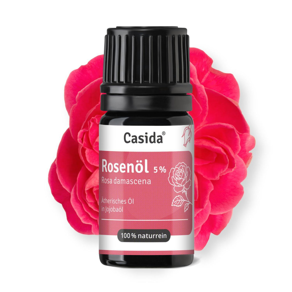 Casida Rosenöl 5 % in dunkler Flasche mit schwarzem Deckel vor einer rosa Rosenblüte