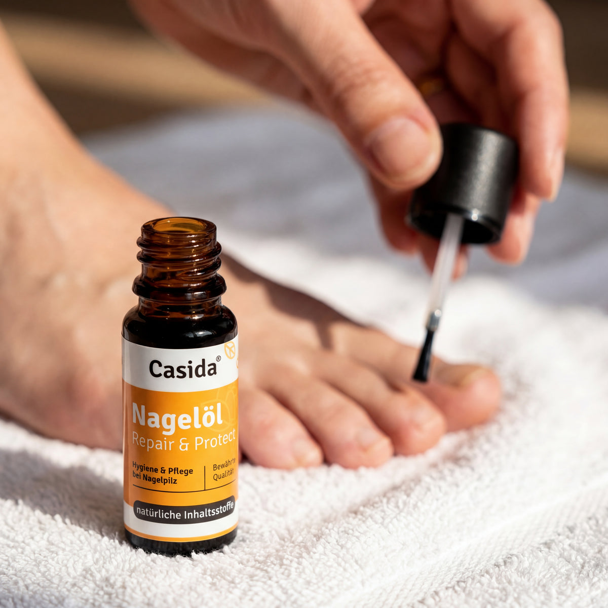 Nagelöl Repair & Protect bottle next to a foot with nail polish being applied on a white towel.