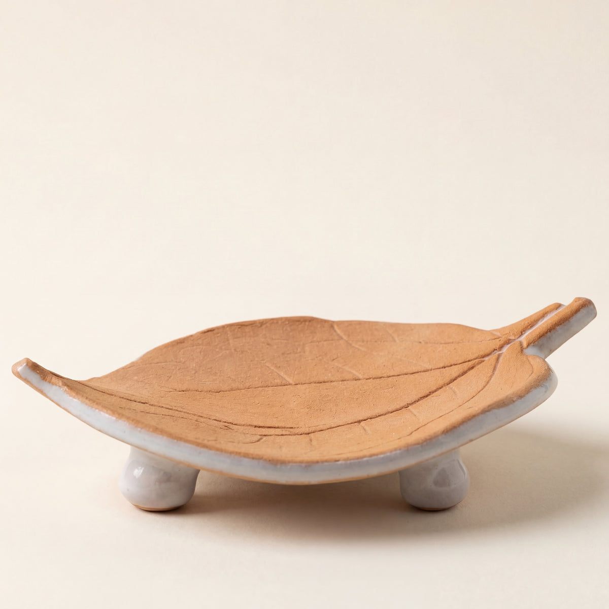 Terracotta-colored ceramic leaf dish with a textured surface and two small feet for support.