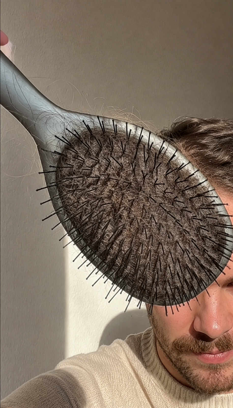 Mann hält eine Haarbürste mit ausgefallenen Haaren vor sein Gesicht.