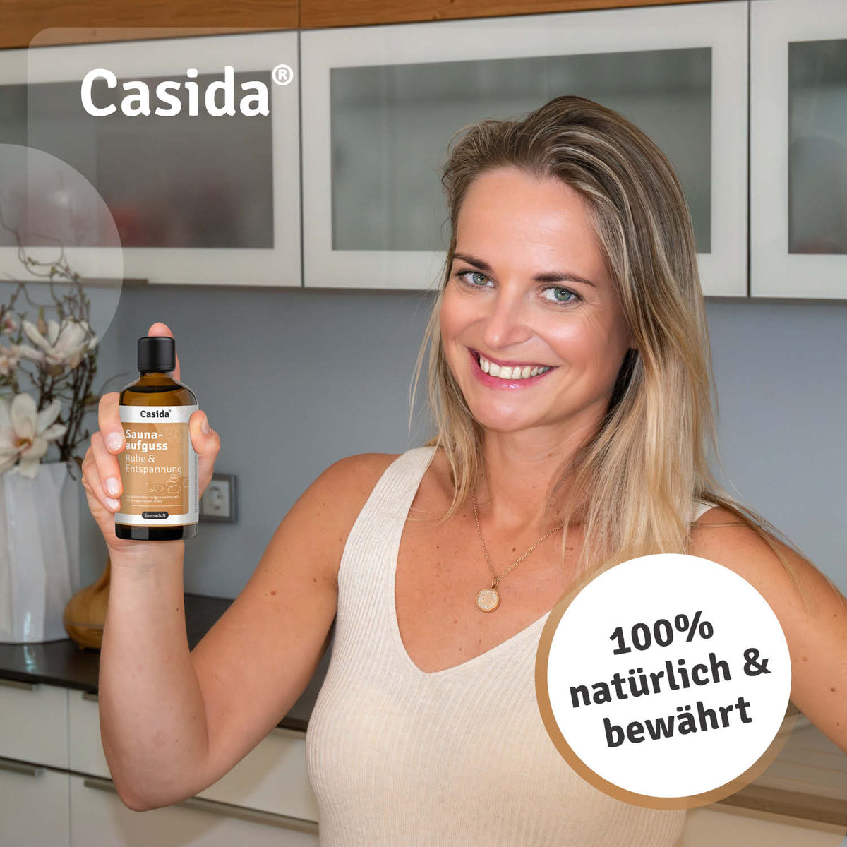 Casida sauna infusion Ruhe & Entspannung oil in a bottle held by a smiling woman in a modern kitchen setting.