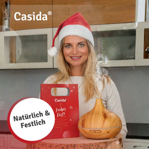Frau mit Weihnachtsmütze präsentiert eine rote Casida Geschenktasche und einen Diffuser in Holzoptik