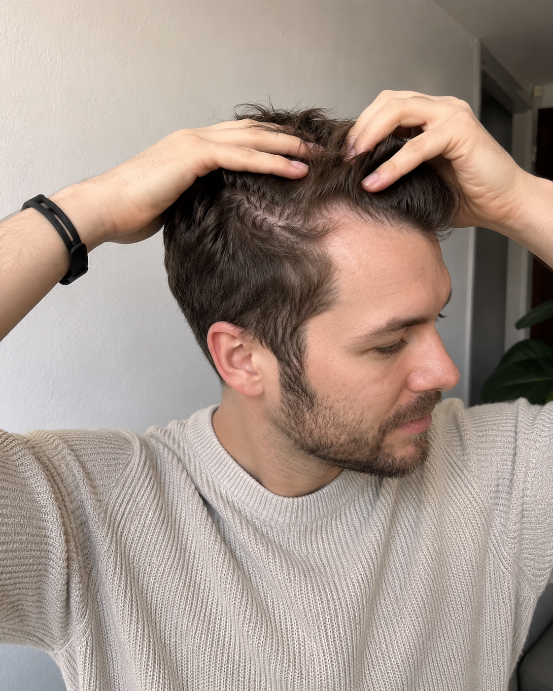 Mann teilt sein Haar mit beiden Händen und zeigt den Scheitel.