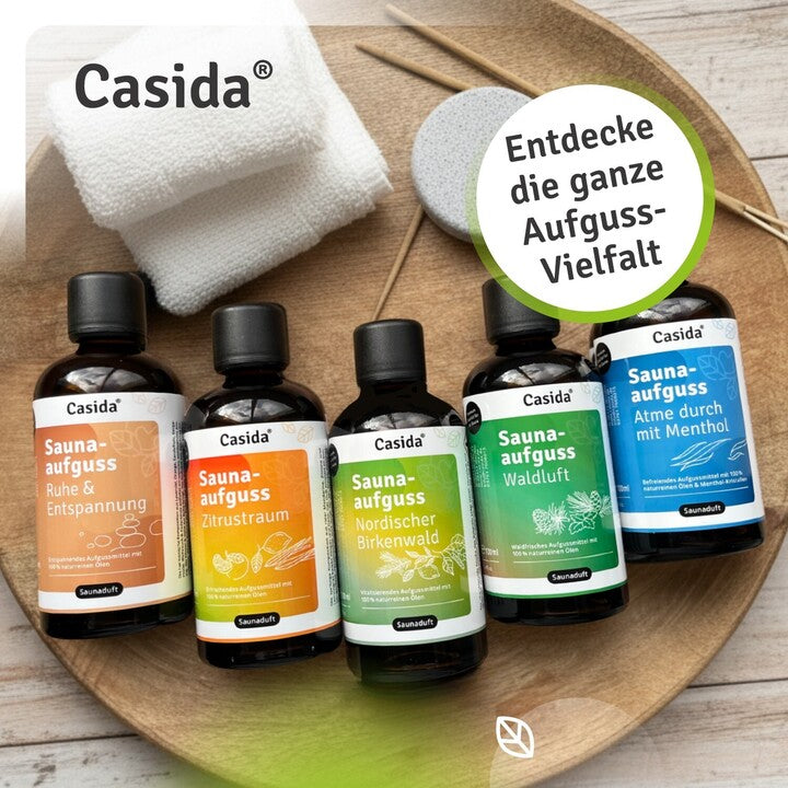 Five bottles of Casida sauna oils in various colors, labeled with scents like Ruhe & Entspannung and Waldluft, on a wooden...